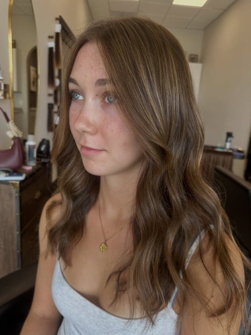Soft brunette with fine golden babylights and long face-framing layers, side view — hair by Alchemy Loft