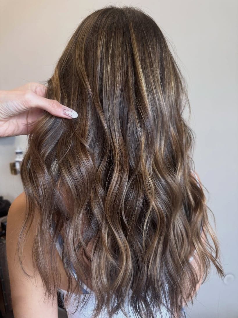 Close look at fine caramel babylights woven through long brunette waves — hair by Alchemy Loft