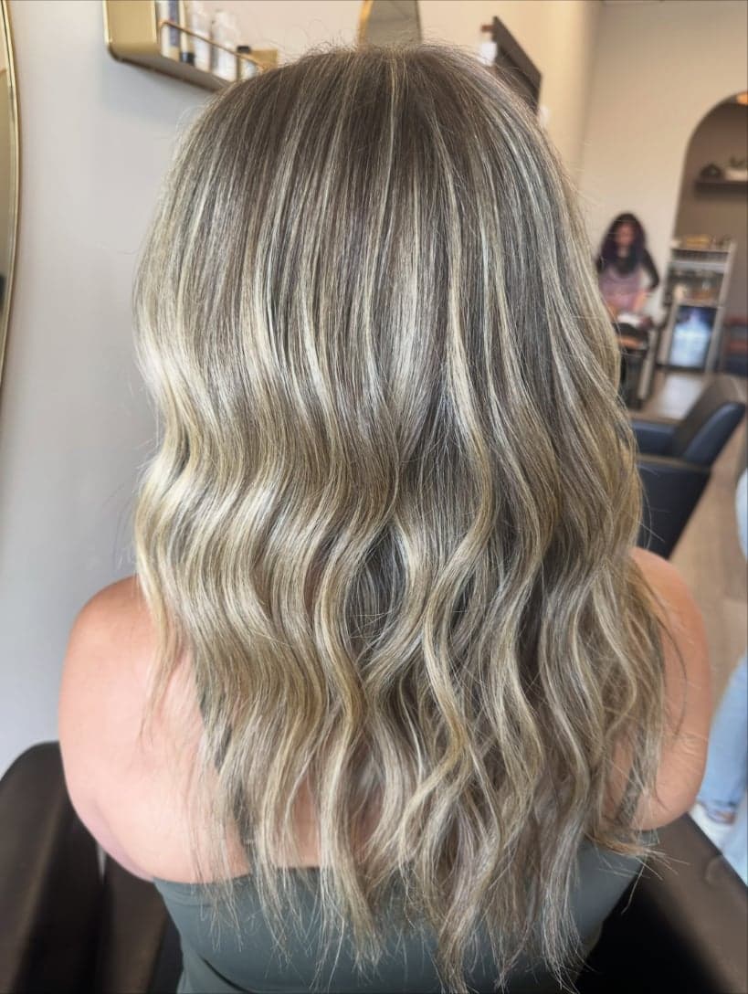 Fine, cool-toned blonde babylights woven through a darker base, shoulder-length waves from the back — hair by Alchemy Loft
