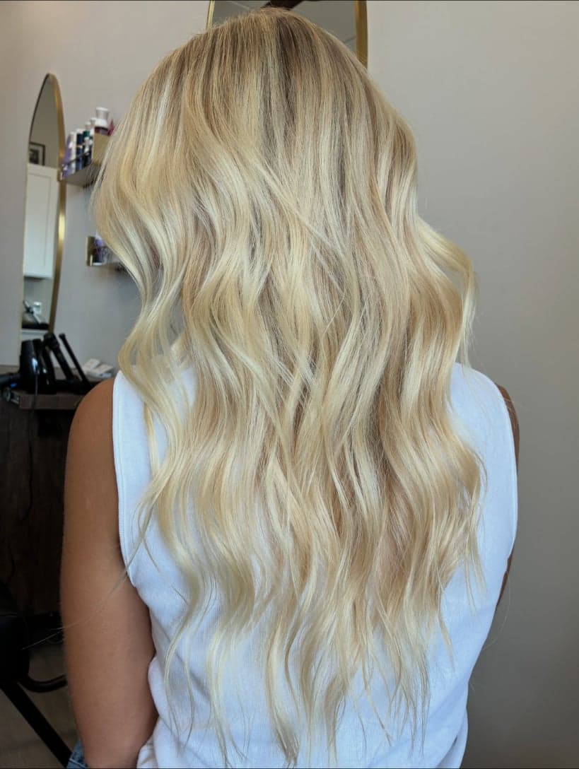 Long, lived-in bright blonde with a softer root, in loose waves, seen from the back — hair by Alchemy Loft