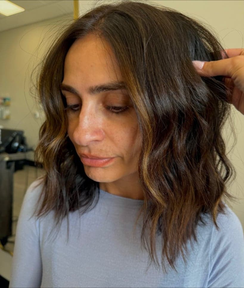 Dark brunette lob in soft waves with warm caramel pieces framing the face — hair by Alchemy Loft
