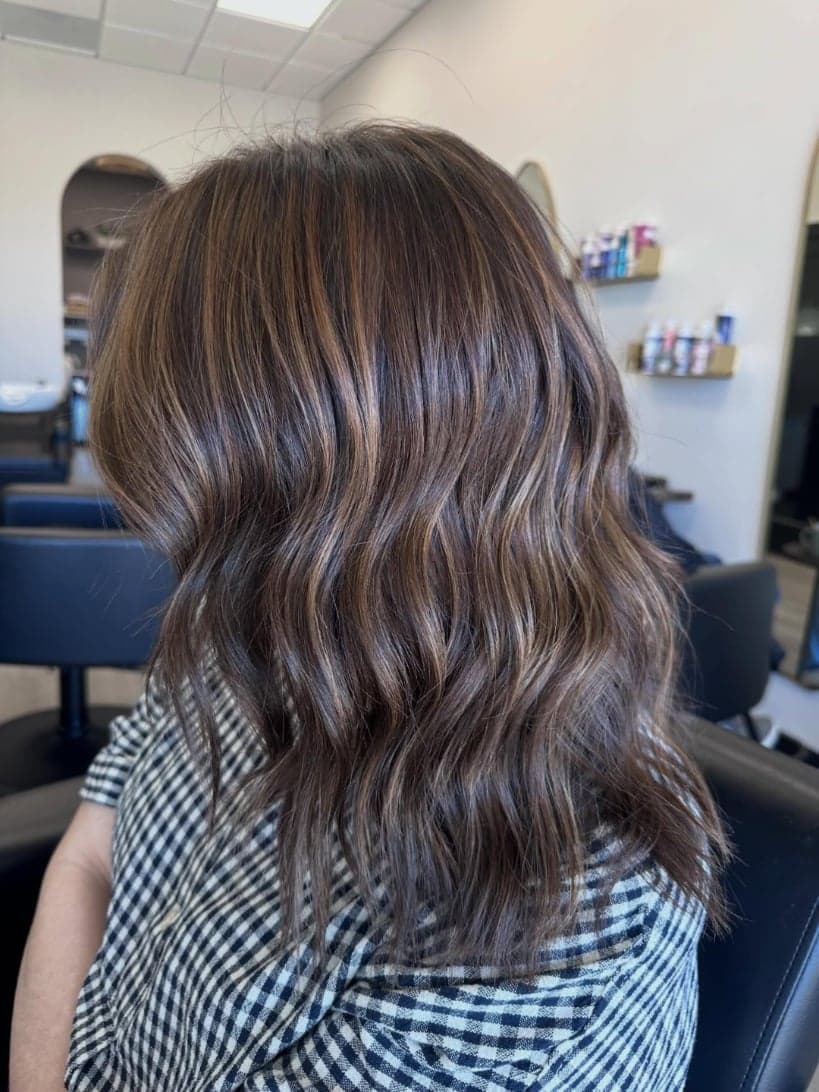 Rich brunette with fine caramel babylights through a wavy shoulder-length cut, back view — hair by Alchemy Loft