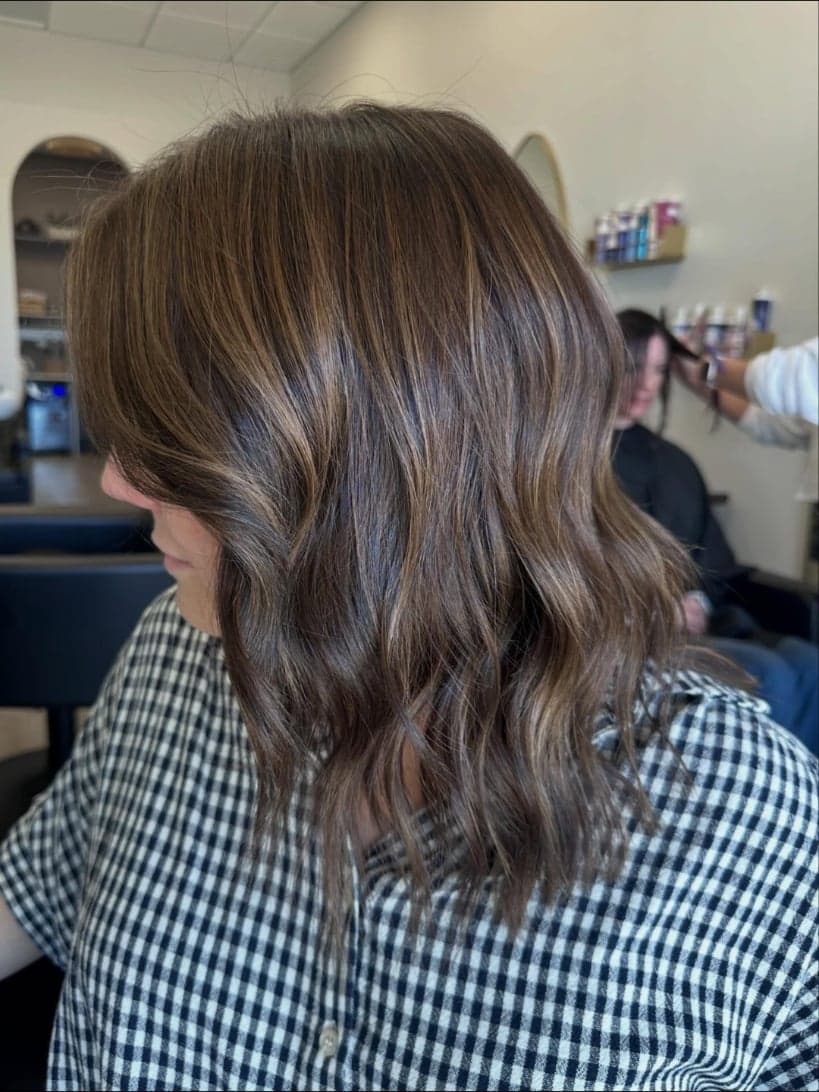 Fine caramel ribbons woven through rich brunette waves, side view — hair by Alchemy Loft