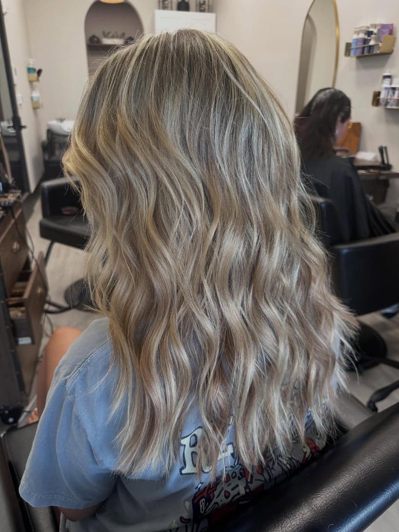 Corrected, blended neutral blonde with a soft root shadow, long waves — hair by Alchemy Loft